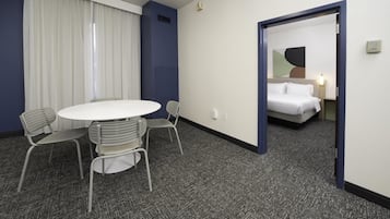 Camera d'albergo con un tavolo rotondo, due sedie, un letto e una porta che conduce a un'altra stanza.