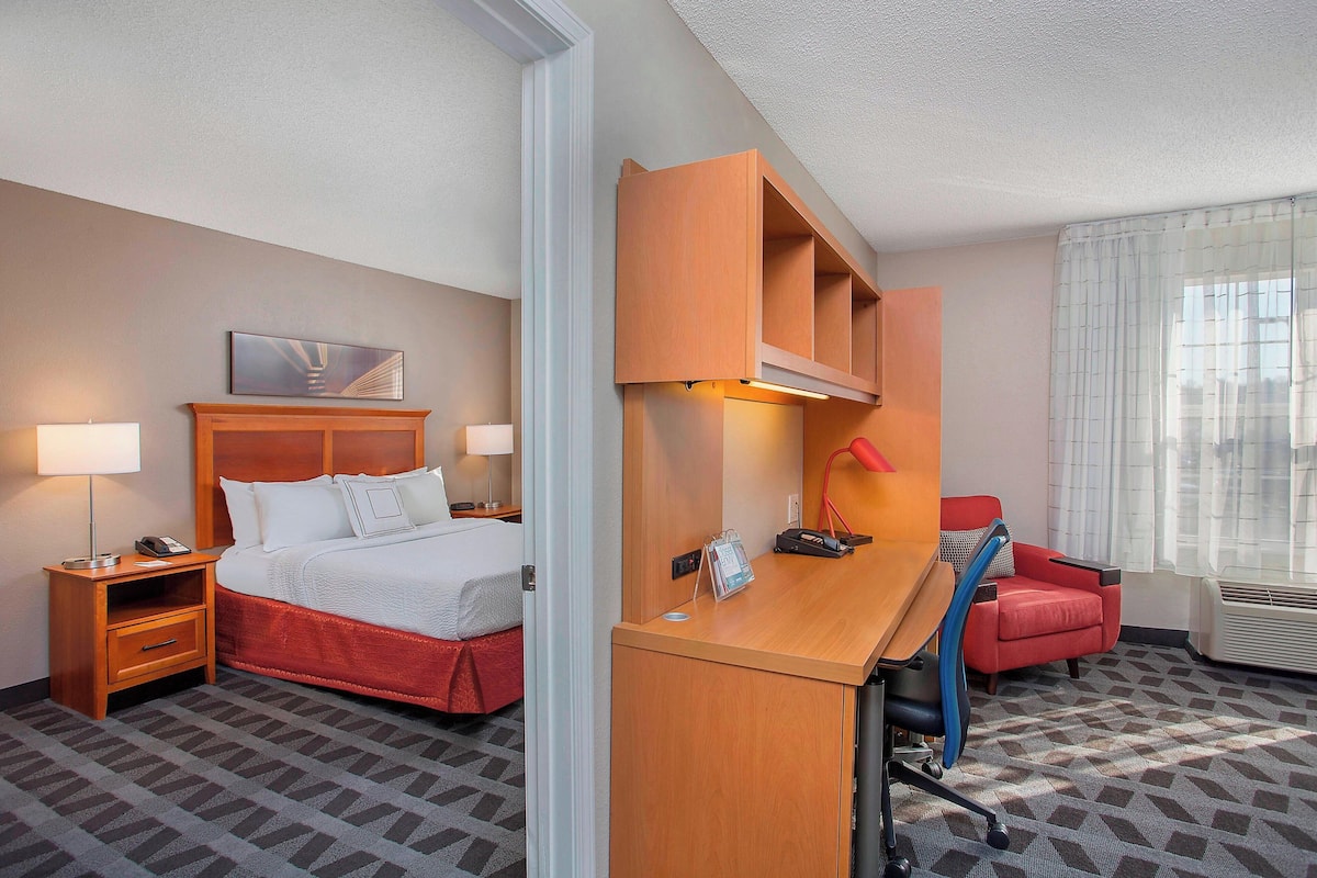 A hotel room with a bed, desk, chair, and a window with curtains.