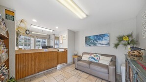 A reception area with a wooden counter, a couch, a painting, and a plant. - Americas Best Value Inn San Clemente Beach (San Clemente)