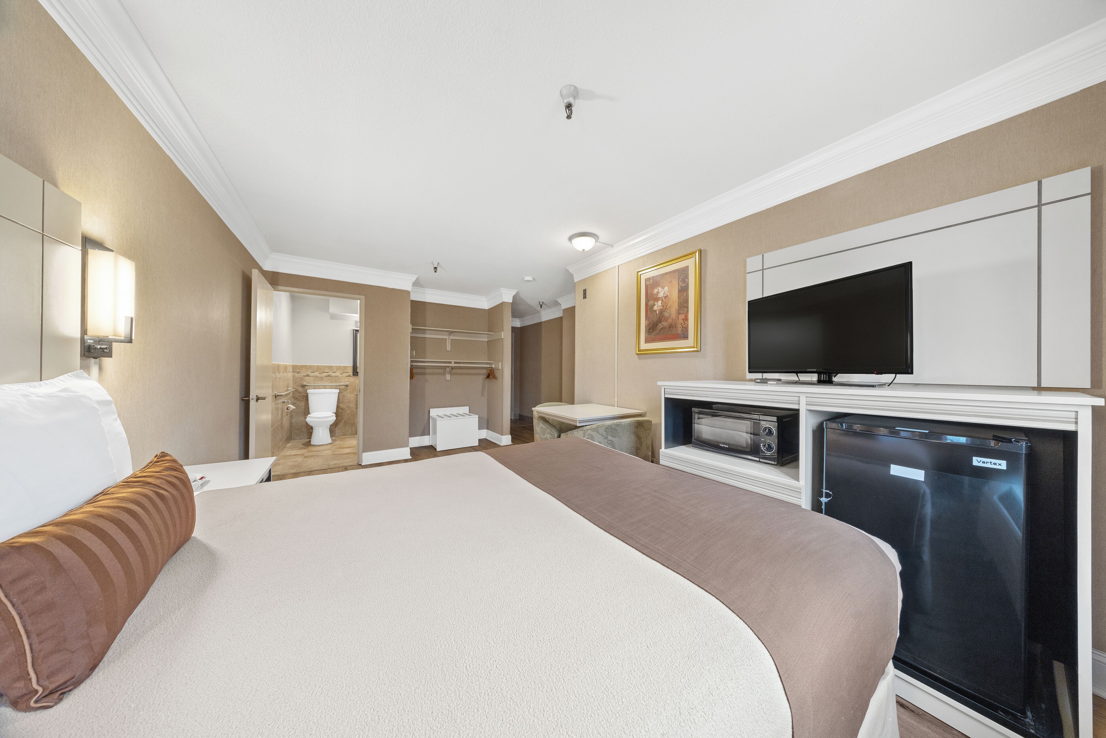 A hotel room with a large bed, a television, a refrigerator, and a bathroom visible through an open door.