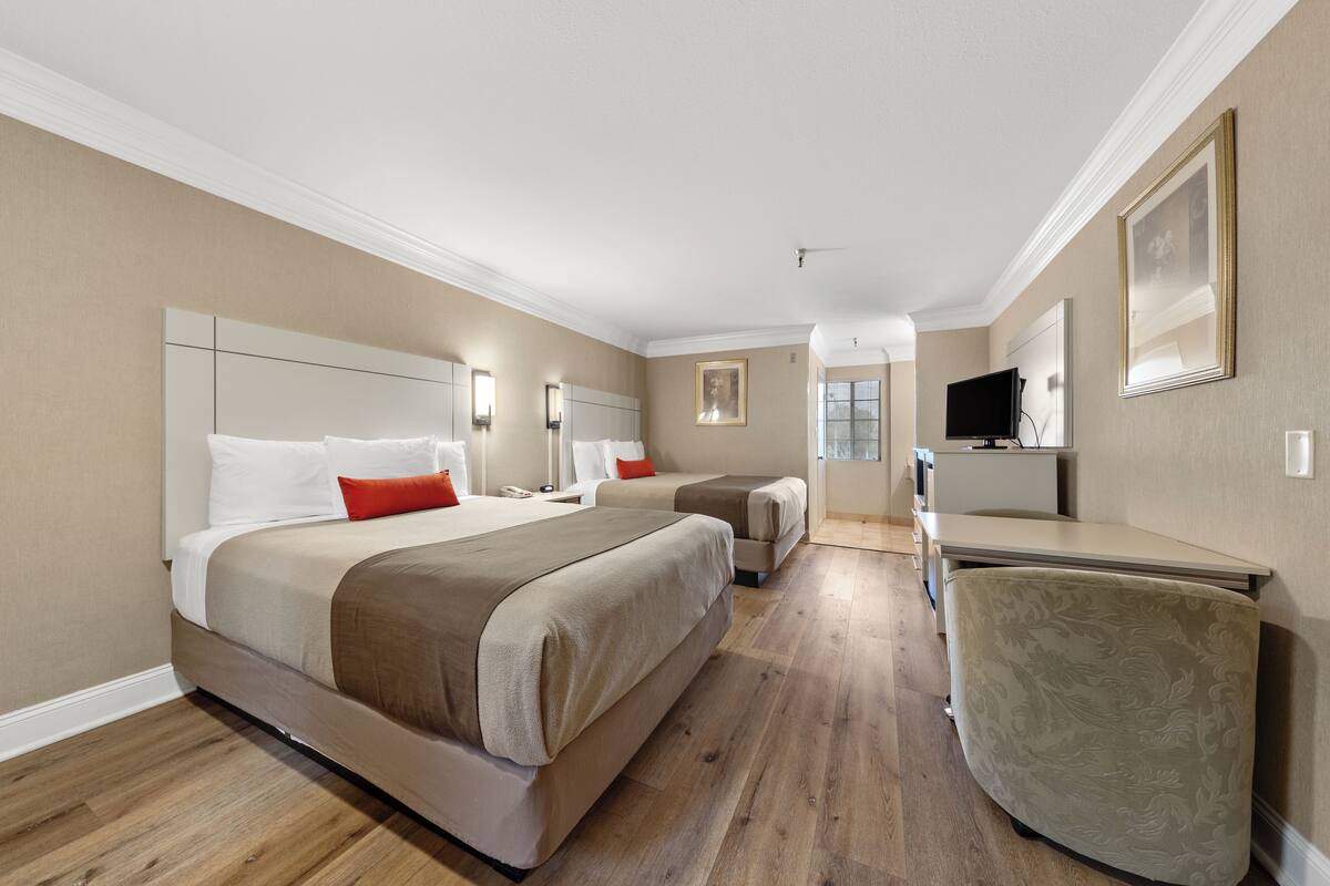 A hotel room with two beds, a desk, a chair, and a television.