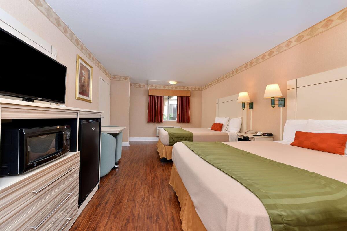 A hotel room with a television, microwave, refrigerator, two beds, a desk, and a window with curtains.