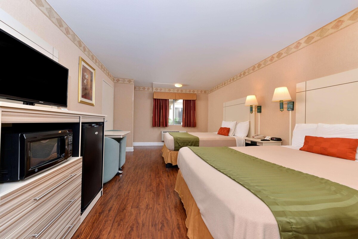 A hotel room with a television, microwave, refrigerator, two beds, a desk, and a window with curtains.