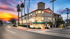 A hotel with a prominent "Budgell Lodge" sign, a corner location with a street view, and a sunset sky. - Americas Best Value Inn San Clemente Beach (San Clemente)