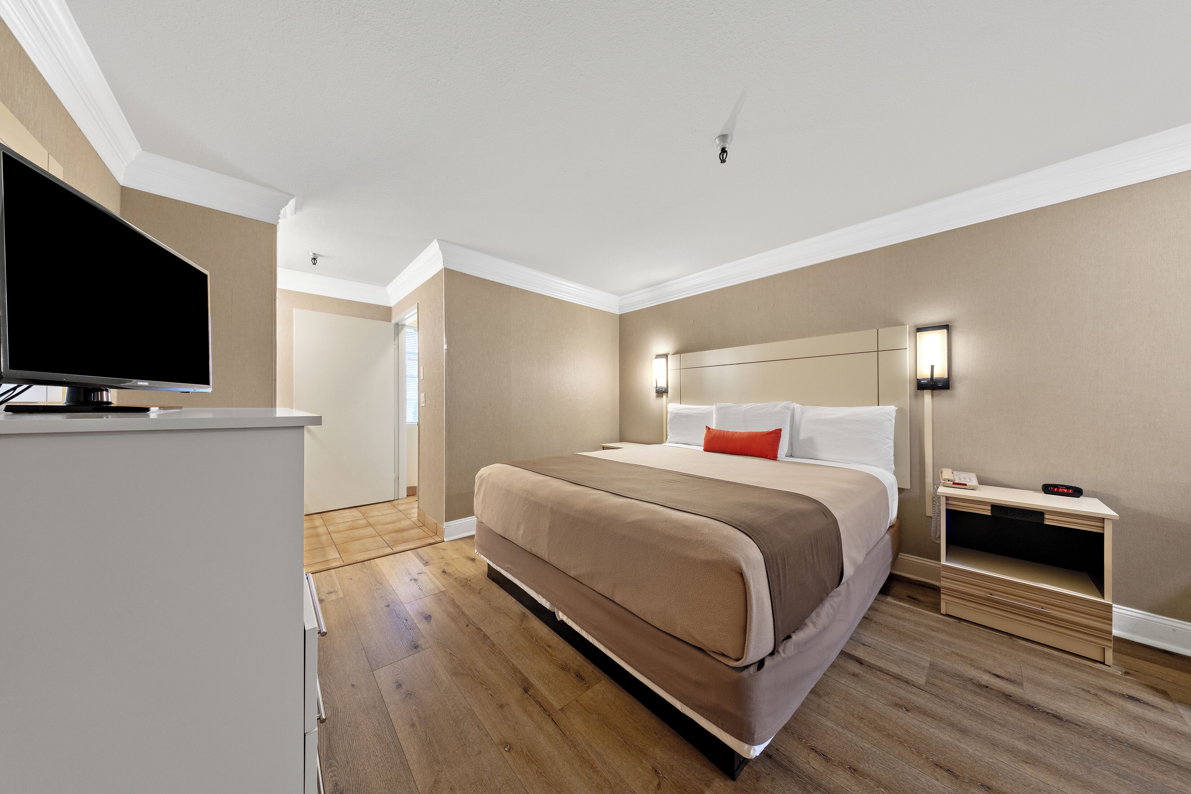 Moderni hotellihuone, jossa on suuri sänky, yöpöytä, televisio ja vaatekaappi.