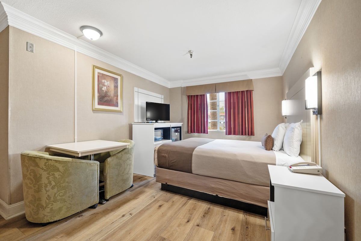 A hotel room with a bed, desk, and chair, a television, and a window with curtains.