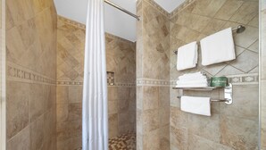 A shower area with a checkered floor, a shower curtain, and a towel rack with multiple towels. - Americas Best Value Inn San Clemente Beach (San Clemente)