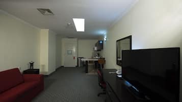 Habitación de hotel con sofá rojo, televisor, escritorio con silla, kitchenette y baño.