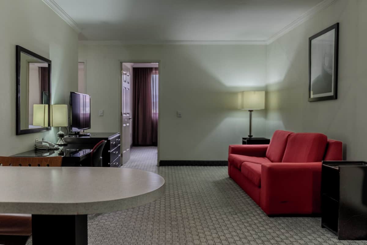 A hotel room with a dining table, a red sofa, a TV, and a lamp.