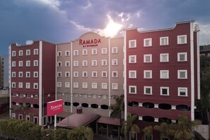 Ein mehrstöckiges Hotel mit einem gut sichtbaren 'RAMADA'-Schild, zahlreichen Fenstern und einem Flachdach.