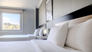 Hotellihuone, jossa on kaksi sänkyä, ikkuna, yöpöytä ja seinään kiinnitetty valaisin.
