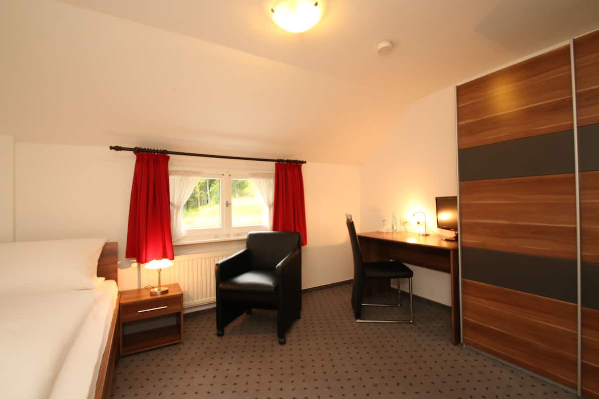 Habitación de hotel con cama, escritorio, silla, mesita de noche y ventana con cortinas.
