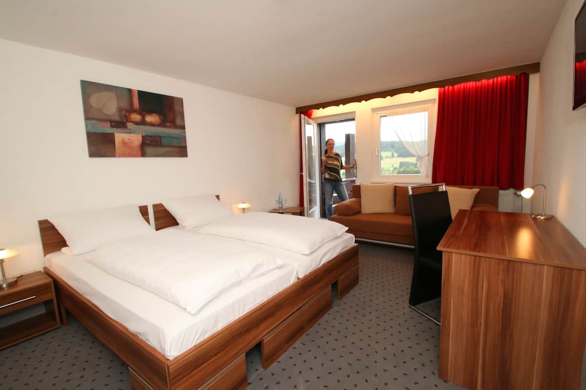 Habitación de hotel con una cama grande, un escritorio de madera, un sofá y una ventana con cortinas rojas.