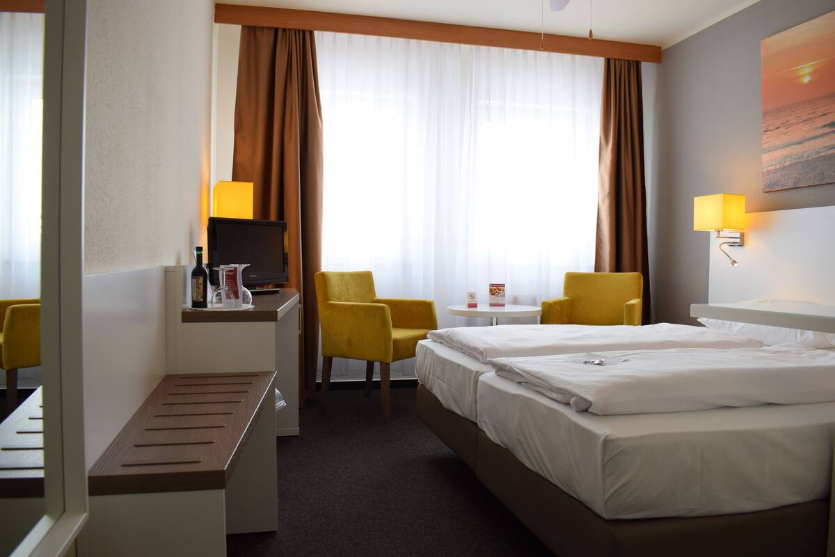 A hotel room with two beds, a desk with a computer, a chair, a small table, and a TV.