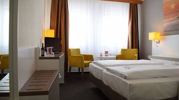 A hotel room with two beds, a desk with a computer, a chair, a small table, and a TV.
