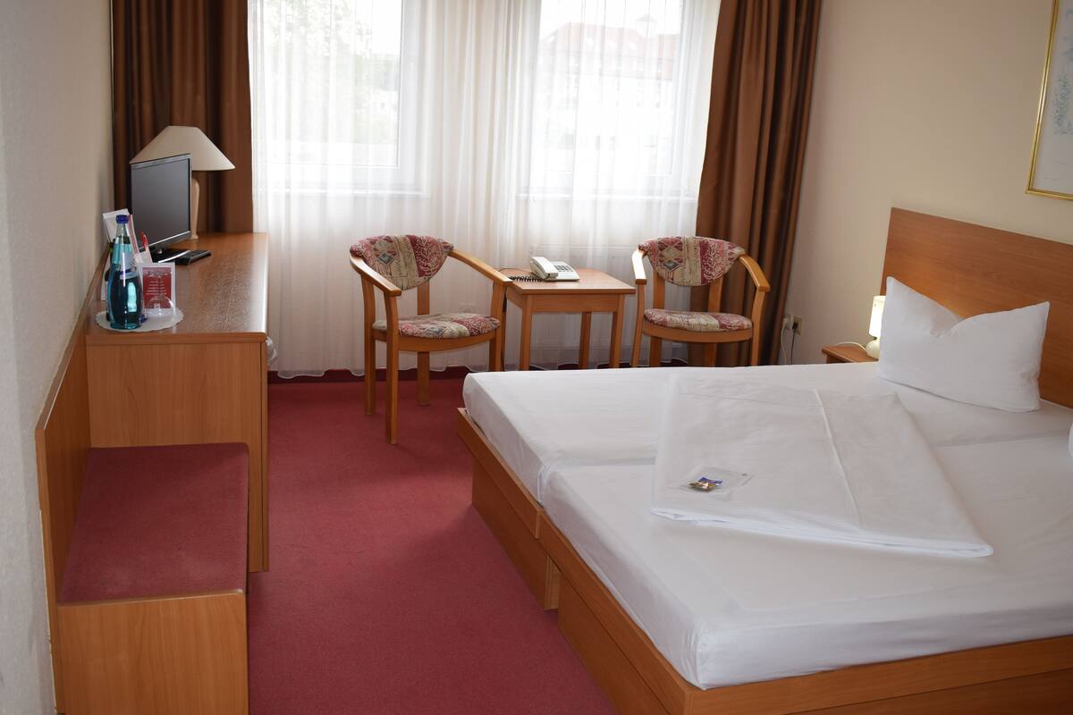 A hotel room with a large bed, two chairs, a small table, a desk with a computer, and a lamp.