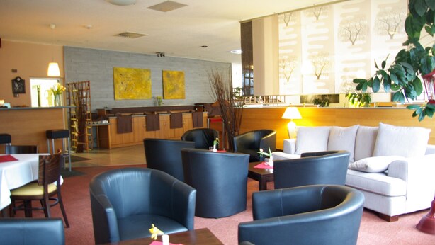 Un vestíbulo de hotel con zonas de estar, un mostrador de recepción y un ventanal con vistas a árboles.