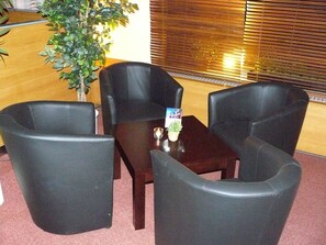 A seating area with three black chairs and a small table, a potted plant, and a wooden reception desk. - astral Inn Hotel Leipzig (Leipzig)