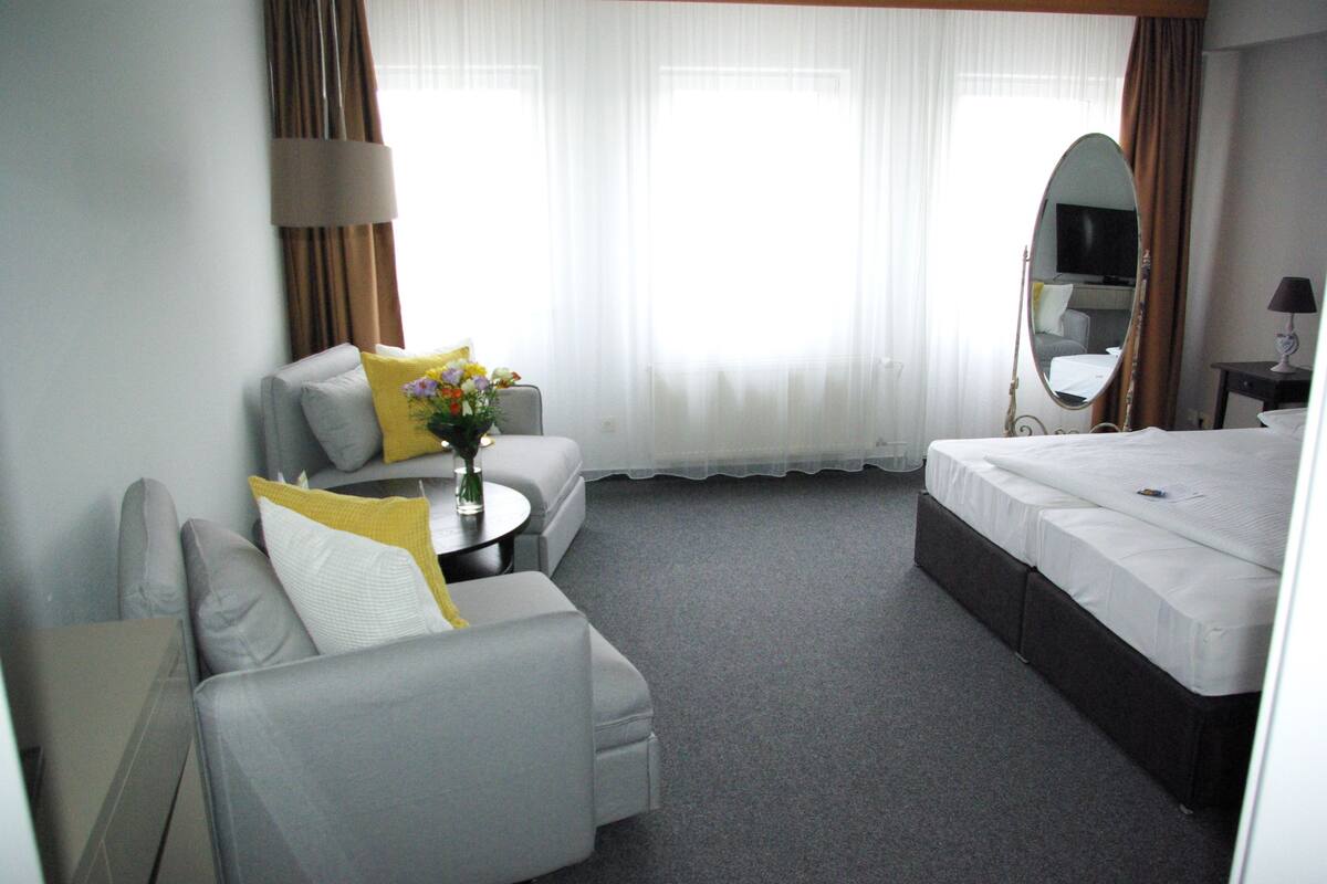 A hotel room with a bed, a sofa, a small table with a vase of flowers, a mirror, and a television.