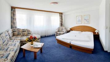 Ein Hotelzimmer mit Bett, einer Couch, einem kleinen Tisch mit Blumenvase und einem Fenster mit Vorhängen.