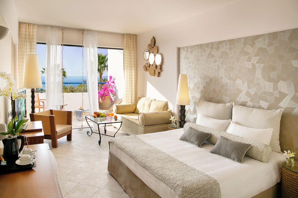 Habitación de hotel con cama, sofá, mesa de centro, una silla y vista al océano.