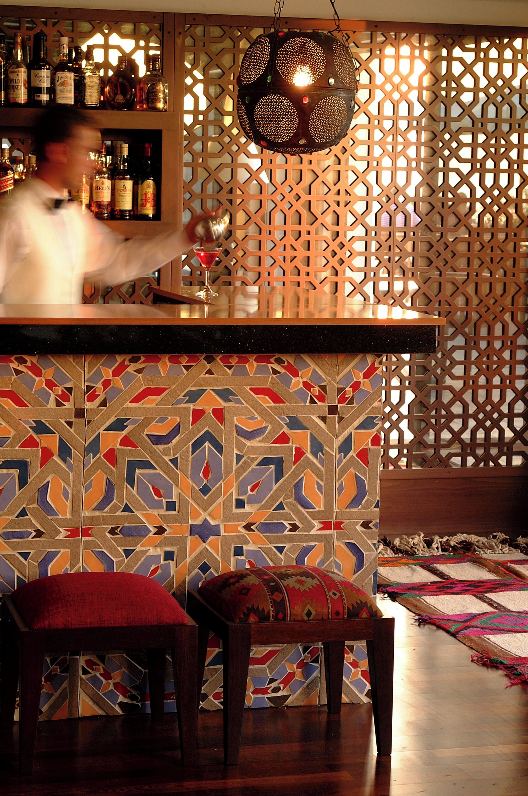Zona de bar con pared decorada, lámpara colgante y barra.