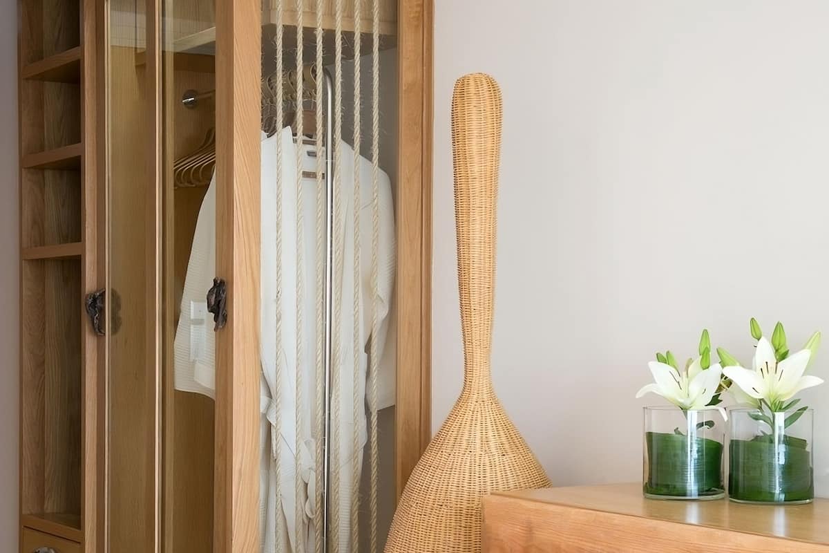 Una habitación con un armario de madera, un jarrón tejido y una mesa con dos jarrones de vidrio con flores.