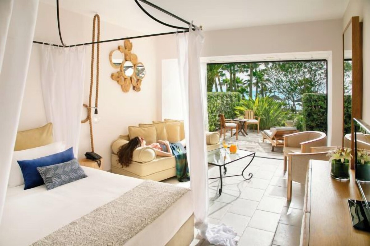 Un dormitorio con una cama, un sofá y una mesa de centro. Cuenta con un balcón con mobiliario exterior.