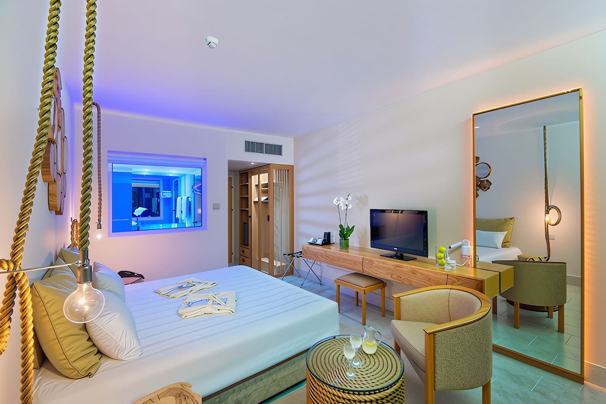 Una habitación de hotel moderna con cama, escritorio, televisión y un espejo grande.