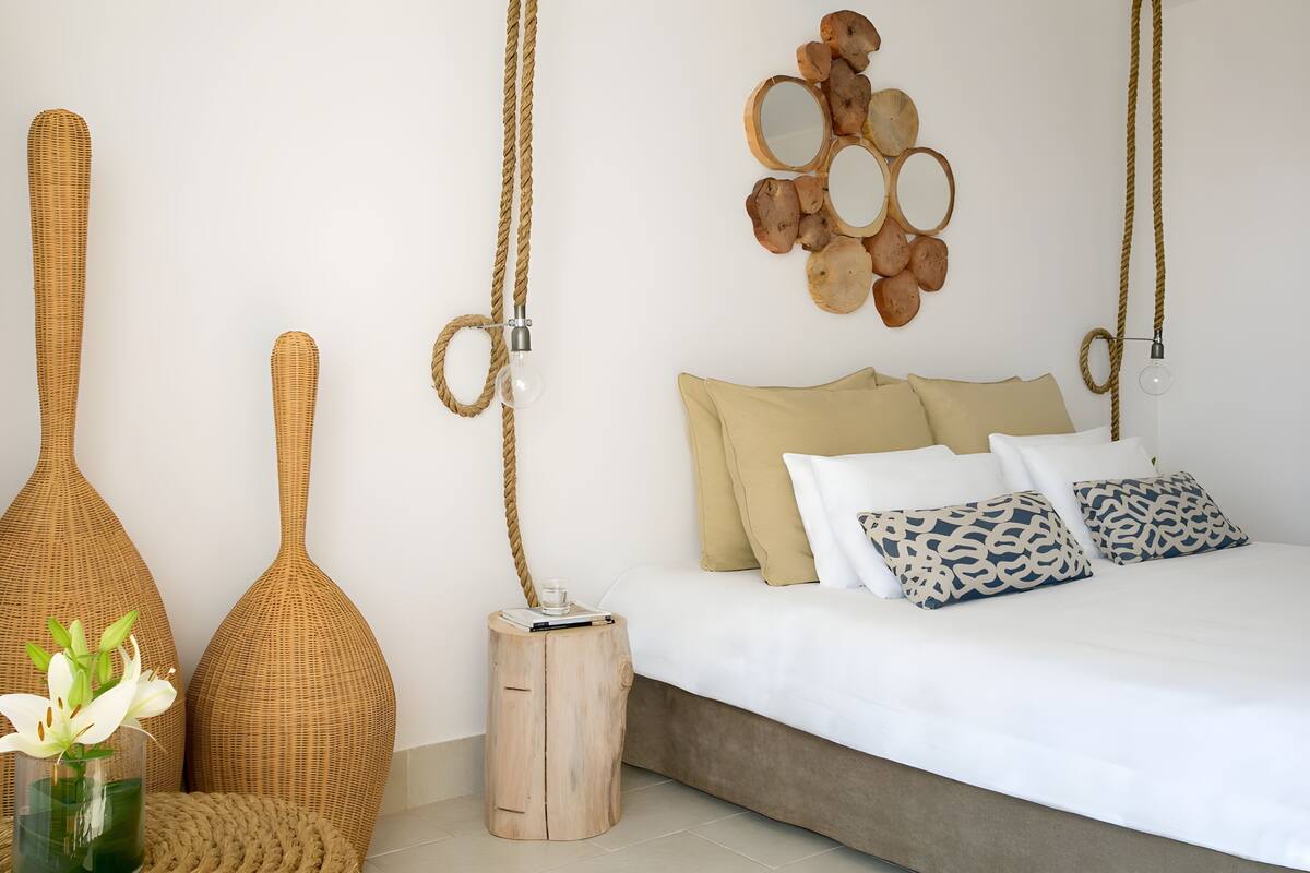 Un dormitorio con cama, almohadas, una mesita de noche con lámpara y decoración en la pared.