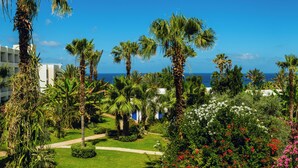 Un exuberante jardín con palmeras, un edificio blanco con cúpula y vistas al mar.