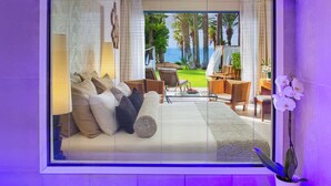 Una habitación con un ventanal grande, un sofá con cojines, una silla, una mesita y una orquídea en maceta.