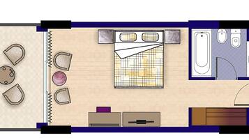 Layout de quarto de hotel com cama, banheiro, pequena área de estar e cozinha compacta.