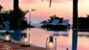 Escena junto a la piscina con sillones de descanso, velas y vistas al atardecer.