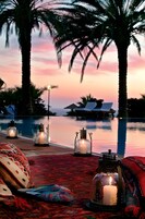Escena junto a la piscina con sillones de descanso, velas y vistas al atardecer.