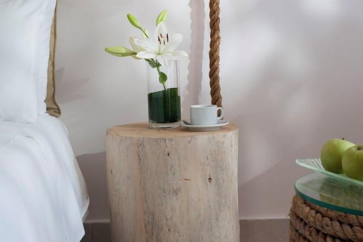 Una mesita de madera con un jarrón de vidrio que contiene una flor blanca y una taza blanca.