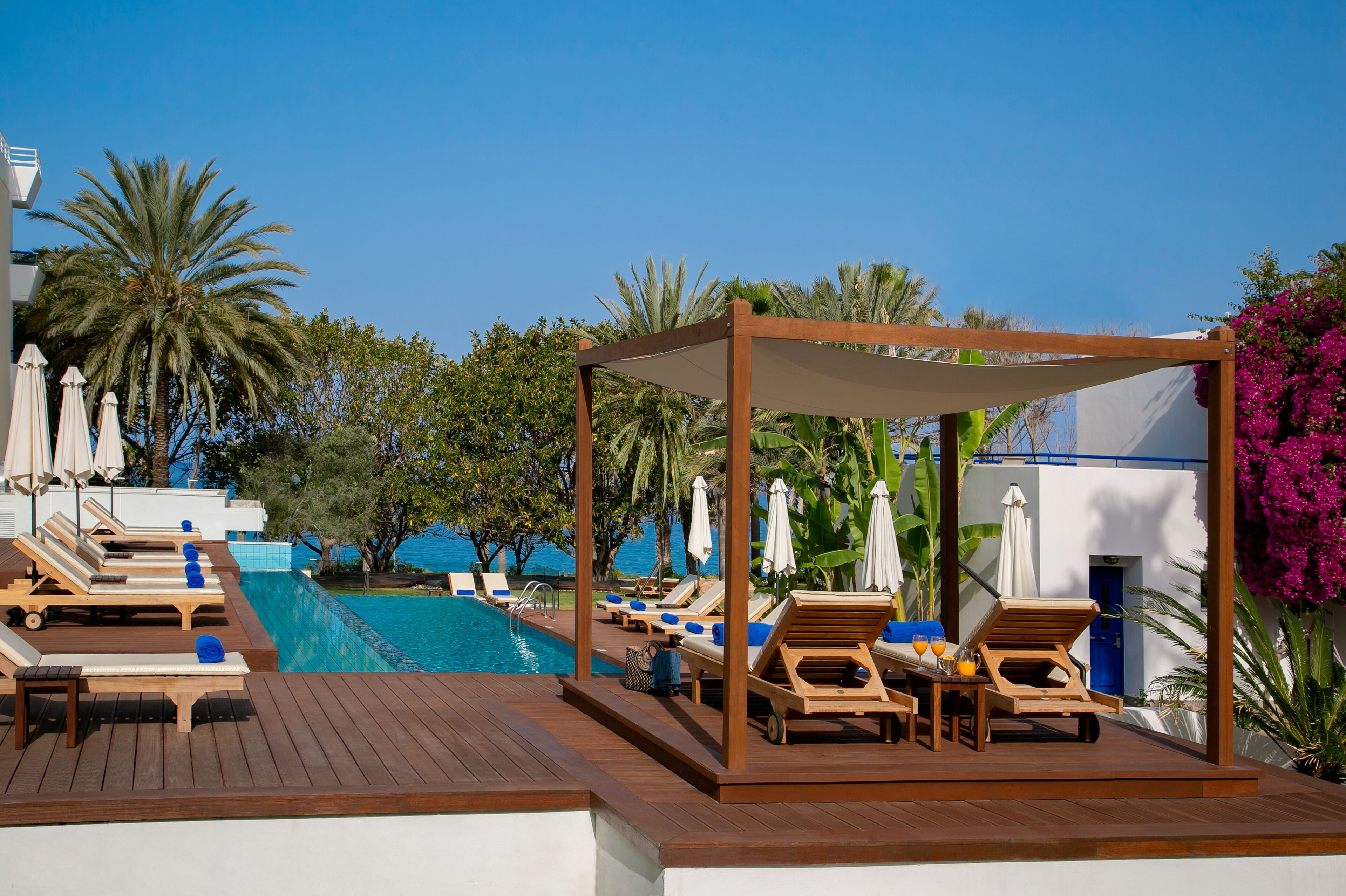 Zona de piscina con tumbonas de madera, un área de estar cubierta y vistas al mar.