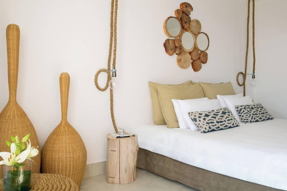 Un dormitorio con cama, almohadas, un espejo montado en la pared y dos grandes jarrones de mimbre.