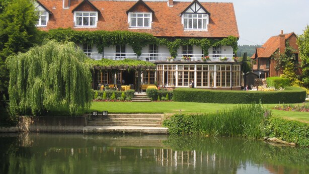 A large, traditional building with a garden and a pond in front.