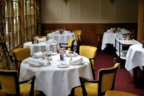 A dining area with round tables set for four, each with white tablecloths, yellow chairs, and neatly arranged table settings including plates, glasses, and cutlery. - French Horn Hotel (Reading)