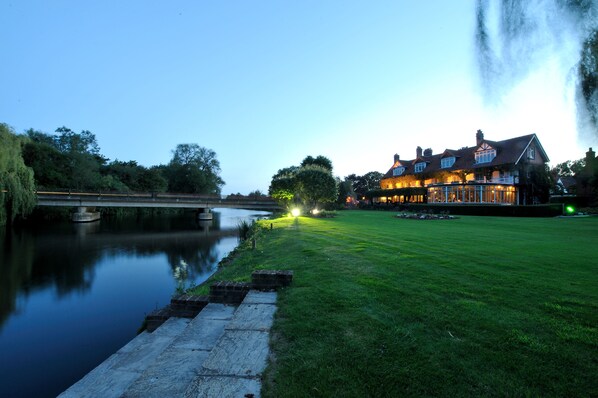 A riverside hotel with a bridge, a well-maintained lawn, and a large building with multiple windows and a chimney. - French Horn Hotel (Reading)