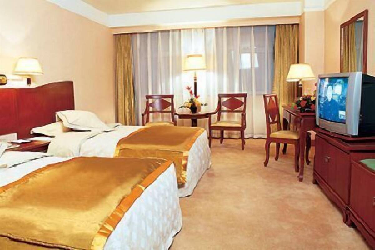 A hotel room with two beds, a desk with a television, and a dining area with chairs and a table.