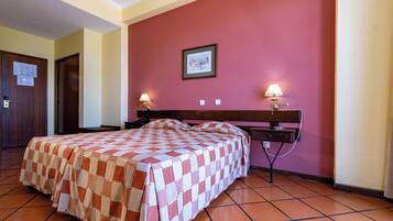 A hotel room with a checkered bedspread, a wooden headboard, two bedside lamps, a framed picture on the wall, and a tiled floor.