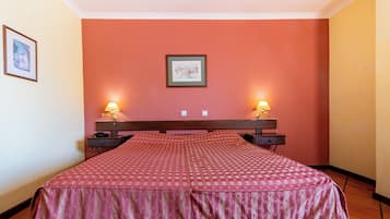 A hotel room with a bed, two bedside tables with lamps, a framed picture on the wall, and a tiled floor.