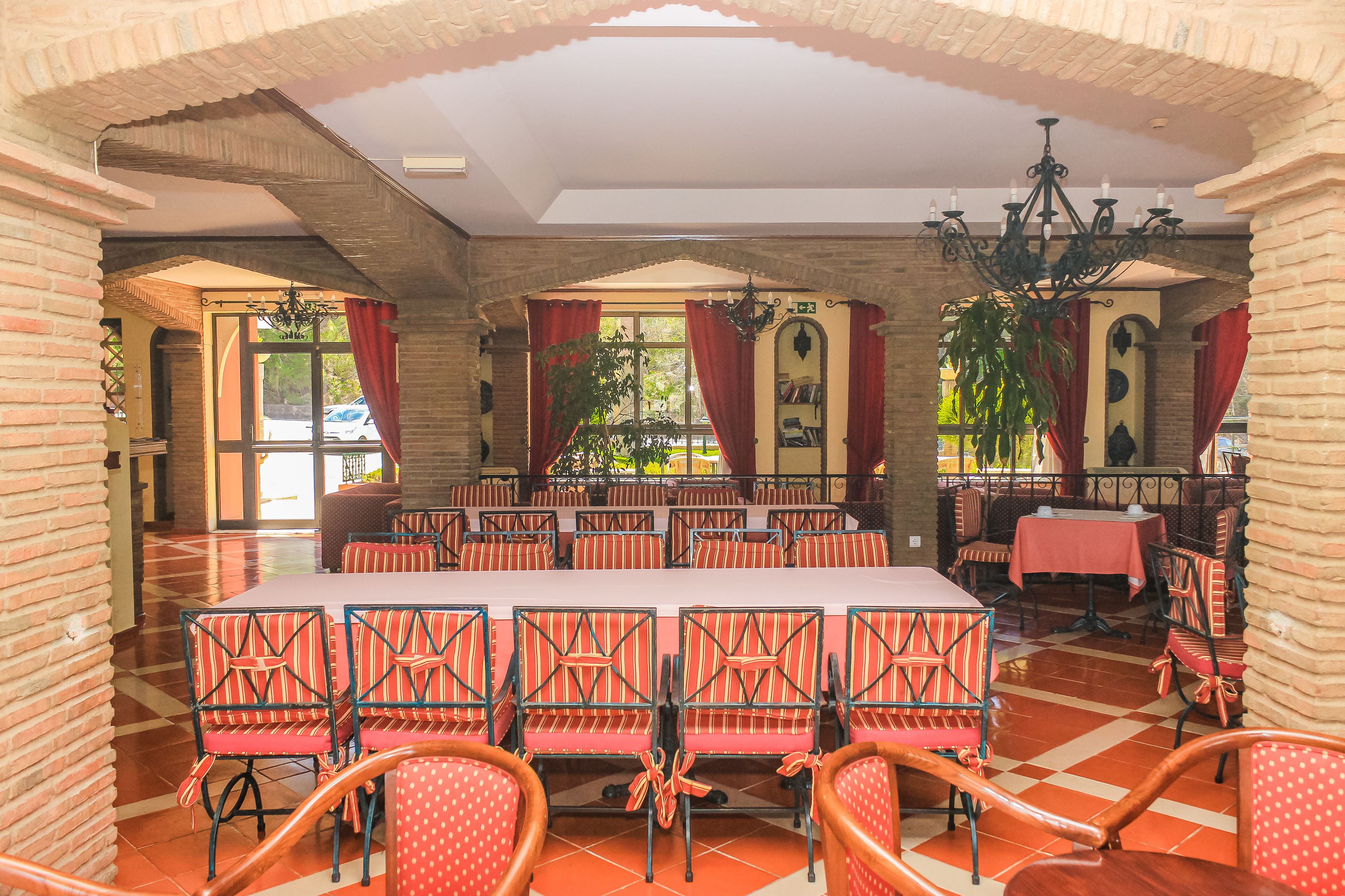 Une salle à manger spacieuse avec des murs en briques, des rideaux rouges et une grande table entourée de chaises à rayures.