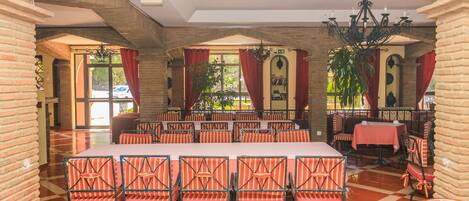 A spacious dining area with brick walls, red curtains, and a large table surrounded by striped chairs.
