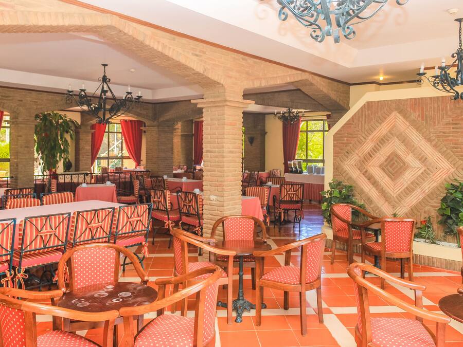 A spacious dining area with multiple tables and chairs, brick walls, and large windows with red curtains.