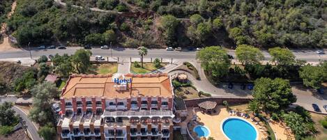 A hotel with a swimming pool, multiple balconies, and a road in the background.