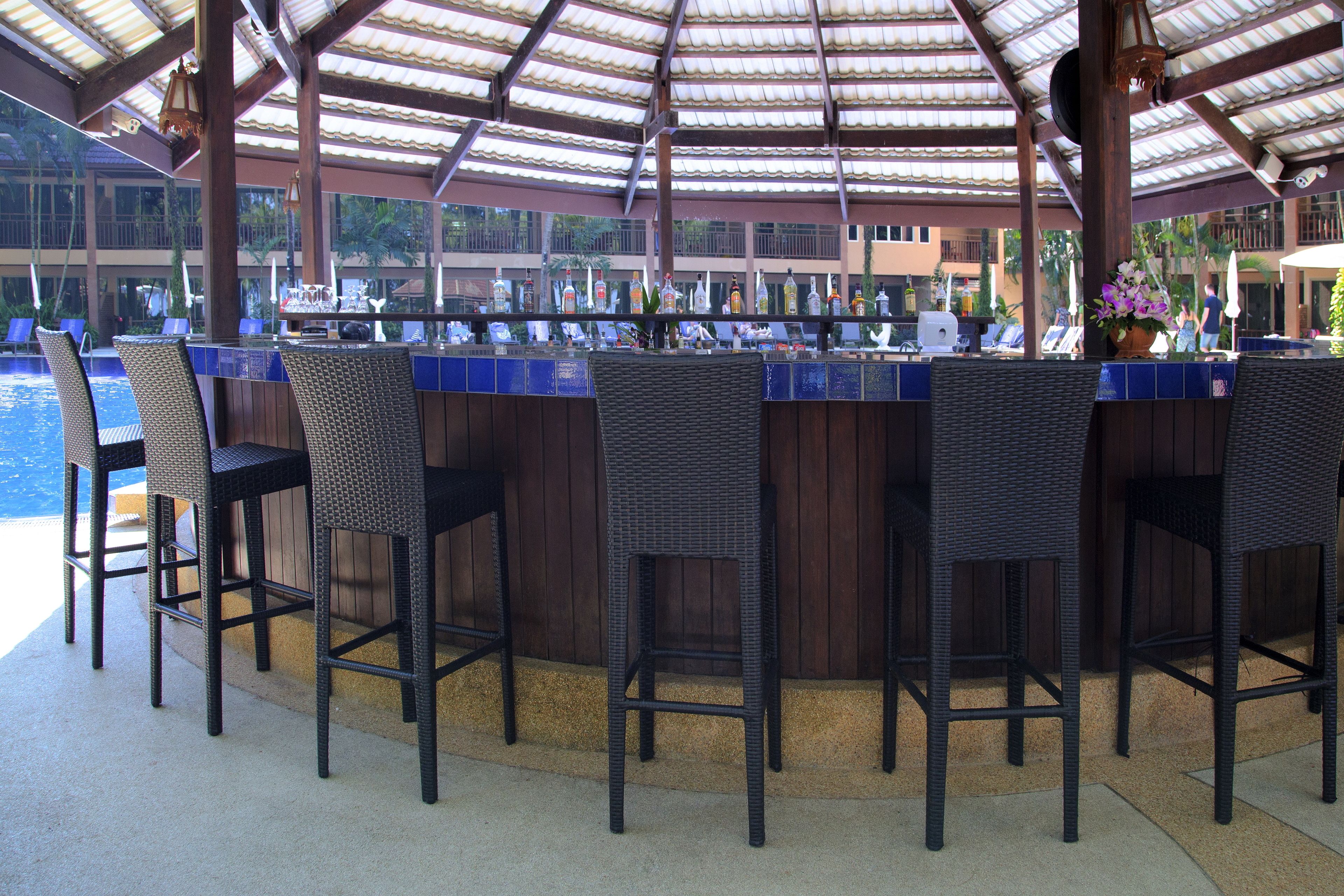 A covered bar area with wicker chairs and a pool in the background.