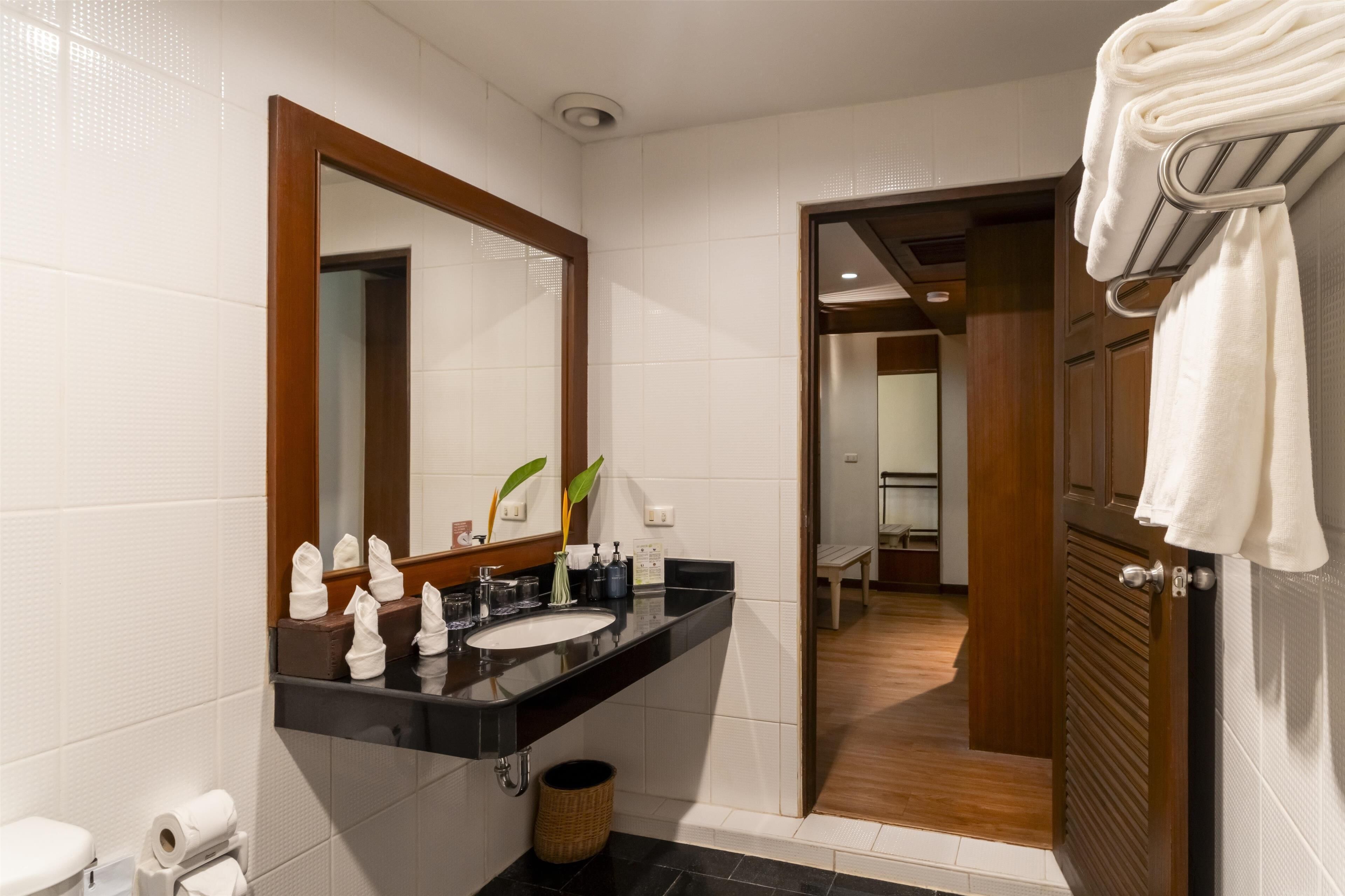 A modern bathroom with a black countertop, a large mirror, and a wooden door leading to a shower area.